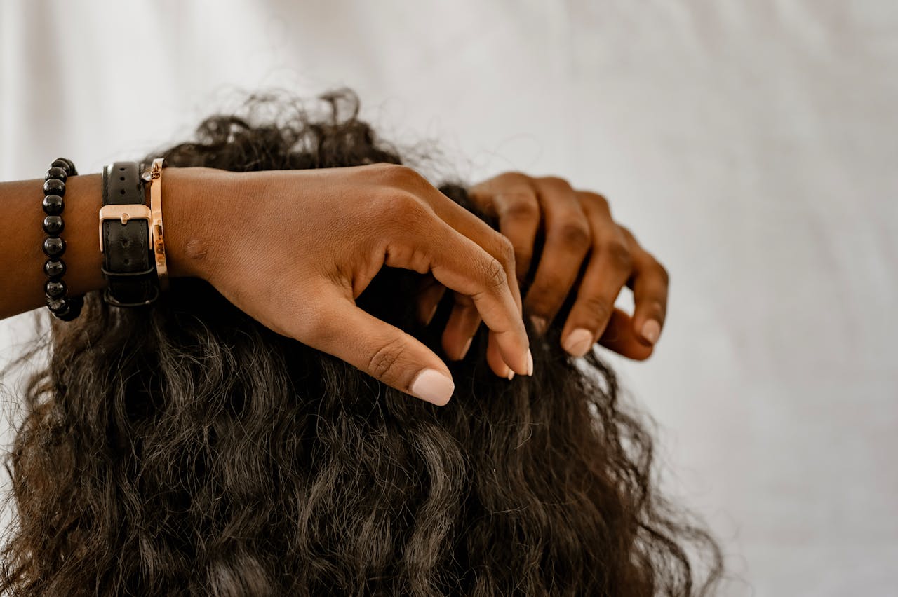 contact-img Detailed image of hands styling curly hair, showcasing accessories and a natural hairstyle.